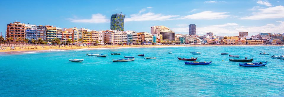 En solig strandpromenad med färgglada byggnader och små båtar i det turkosblå havet.