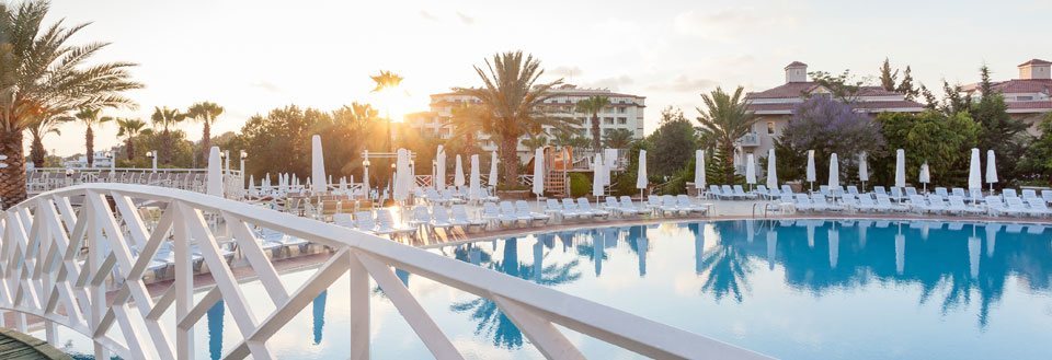 Solnedgång vid ett fridfullt resort i Side med pool, vita solstolar och palmer.