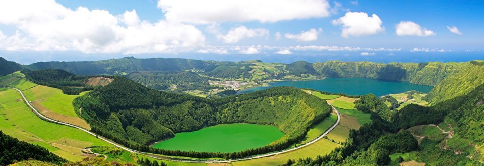 Panoramavy över frodiga, gröna vulkaniska kratersjöar omgivna av skogsbeklädda kullar.