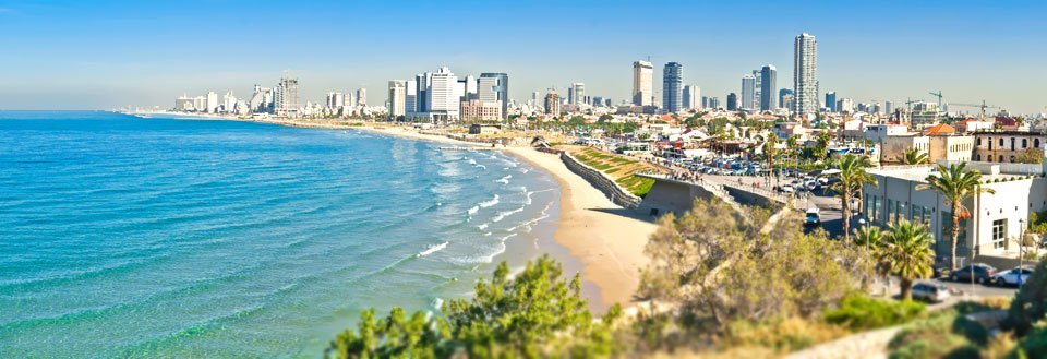 Panoramavy över en kuststad med höghus längs strandpromenaden och klart blått hav.