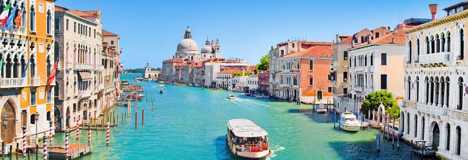 Bilden visar en solig dag i Venedig med historiska byggnader längs Canal Grande och en båt på vattnet.