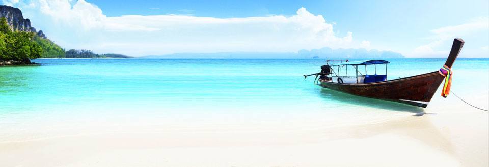 En traditionell långsvansbåt vid en vacker tropisk strand med kristallklart vatten och blå himmel.