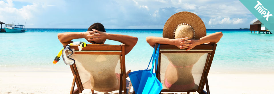 Två personer vilar på solstolar vid en turkos strand med snorkelutrustning och en strandväska.