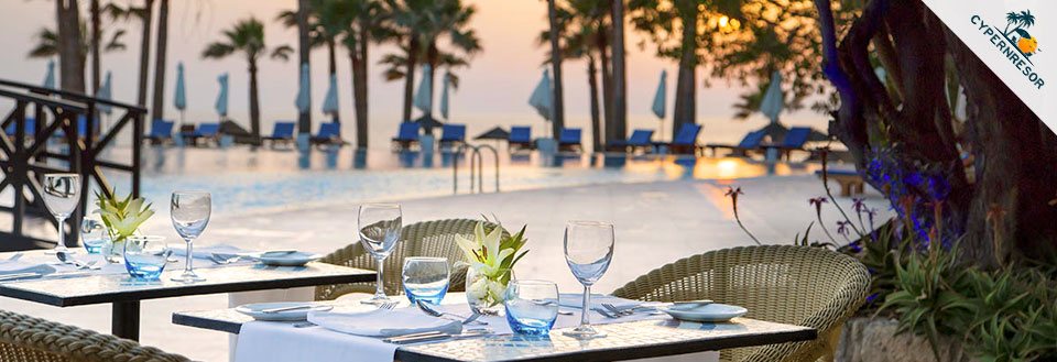 En romantisk middagsmiljö utomhus med dukade bord vid en pool i skymningen, med palmer i bakgrunden.