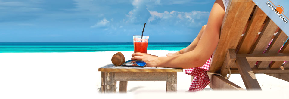 En person vilar på en trä solstol på stranden med en svalkande drink och utsikt över det turkosblå havet.