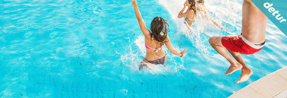 Två personer tar ett hopp i en pool, vilket skapar plask. Det är sommar och glädje.