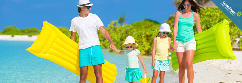 En familj tillbringar en solig dag på stranden med turkosblått vatten och vit sand. De bär badkläder och solhattar.