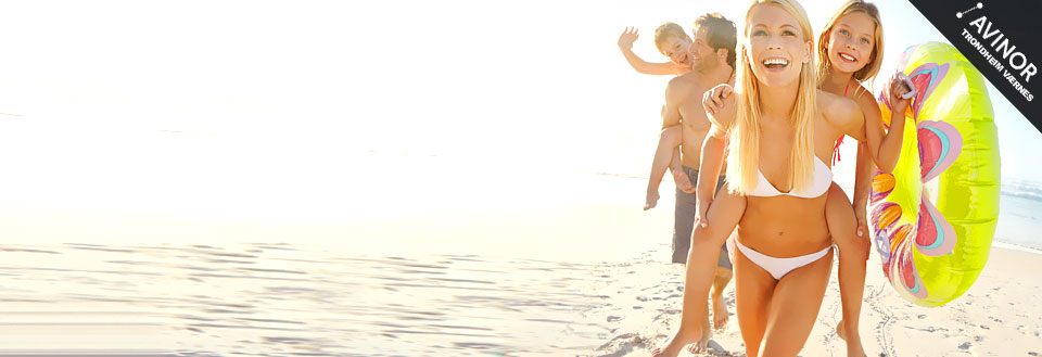 En familj njuter av solen på stranden; barnen leker och en kvinna ler med badkläder och badring.
