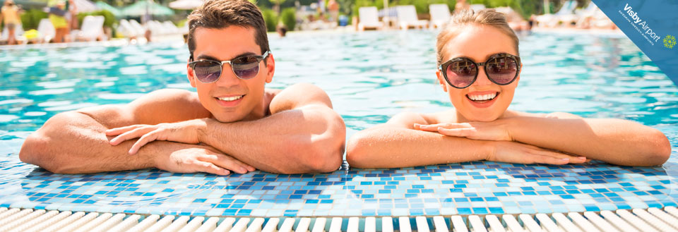 Två leende personer med solglasögon kopplar av i en simbassäng på en solig dag.