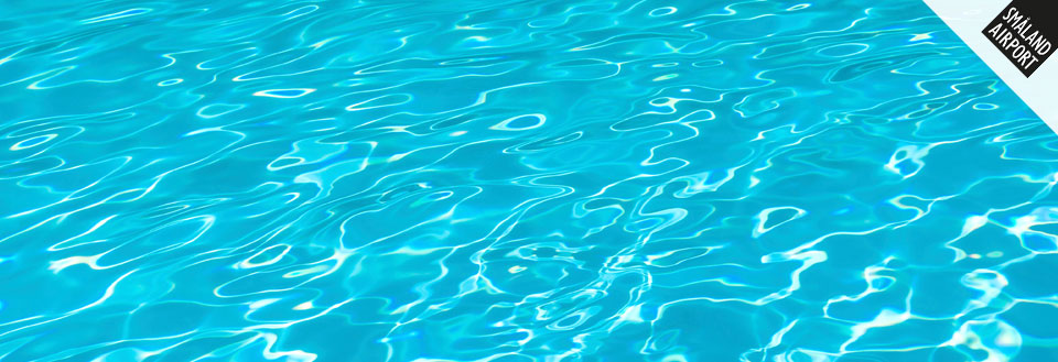 Bilden visar en simbassängs lugna, glittrande yta med klart blått vatten.