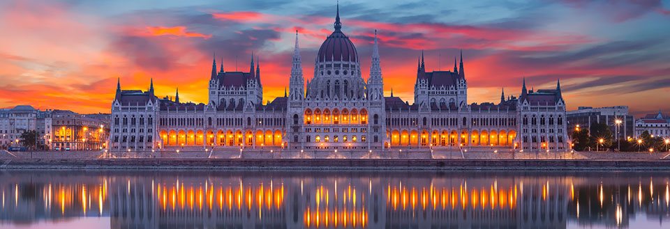 Bilden visar Ungerns parlament i Budapest vid solnedgången med speglingar i vattnet.