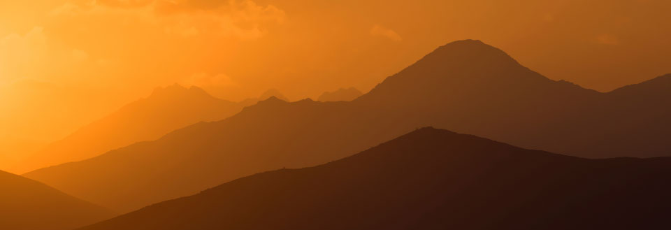 Bilden visar konturerna av bergskedjor mot en gyllene solnedgång med varma färger.