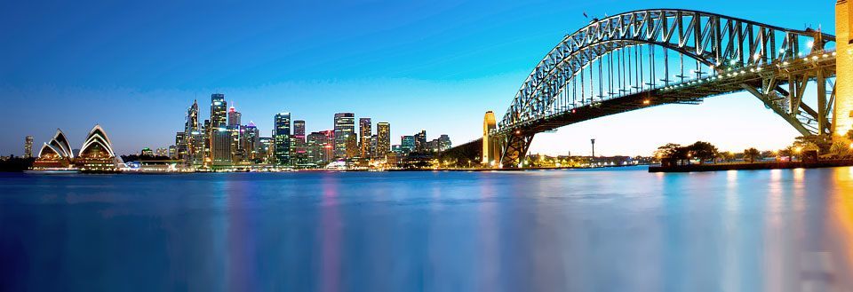 Panoramavy over Sydney med Sydney Bridge och Utzons operahus vid skymning.