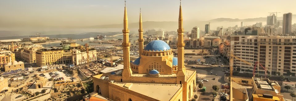 Bild av en stadssilhuett med en framträdande moské och två gyllene minareter under en klar himmel.