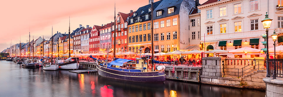 Bild av Nyhavn i Köpenhamn vid skymning med färgglada byggnader och båtar längs kanalen.