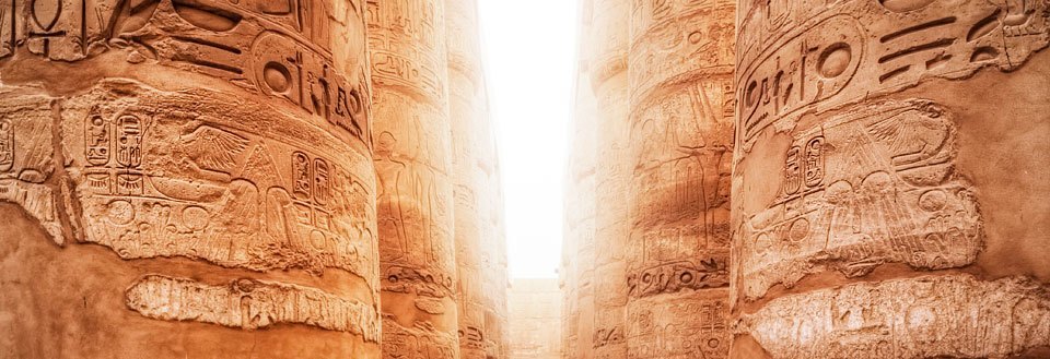 Bilden visar gamla hieroglyfer på pelarna i ett egyptiskt tempel i gyllene ljus.
