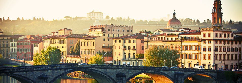 Solnedgang over Arno-elven i Firenze med en steinbro i forgrunnen og historiske bygninger i bakgrunnen.