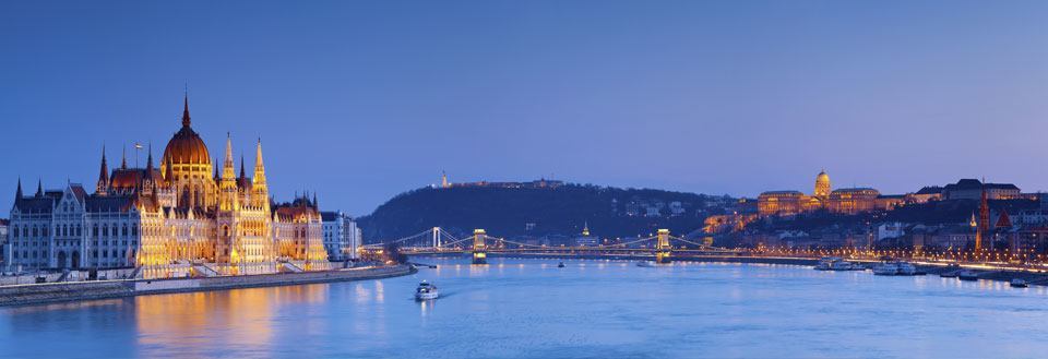 Kvällsbild av en flod i en europeisk stad med upplysta byggnader och en bro.