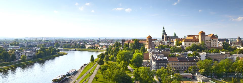 Panoramavy över en europeisk stad med historiska byggnader och ett slott vid en flod omgiven av grönområden.
