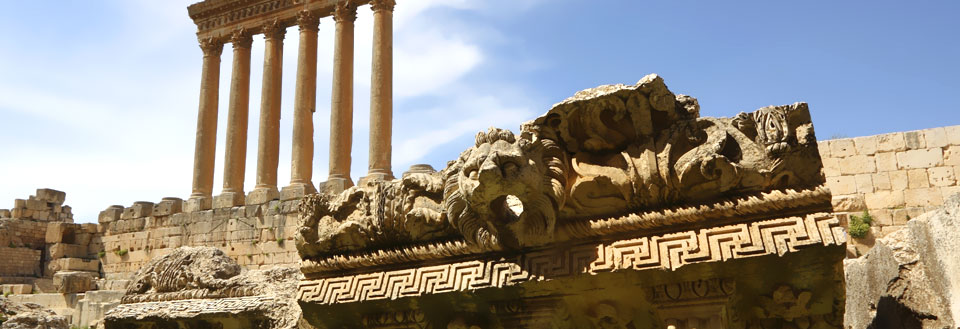 Antika ruiner med pelare och detaljerad stenskulptur under en klarblå himmel.