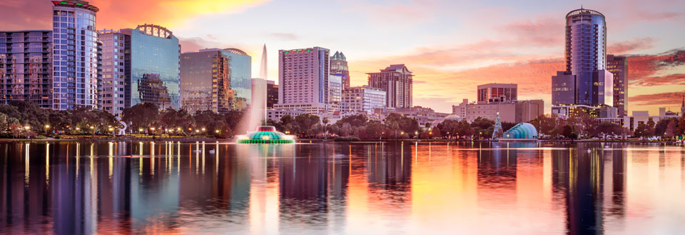 Orlandos skyline vid solnedgången med byggnader som speglar sig i ett lugnt vattendrag.