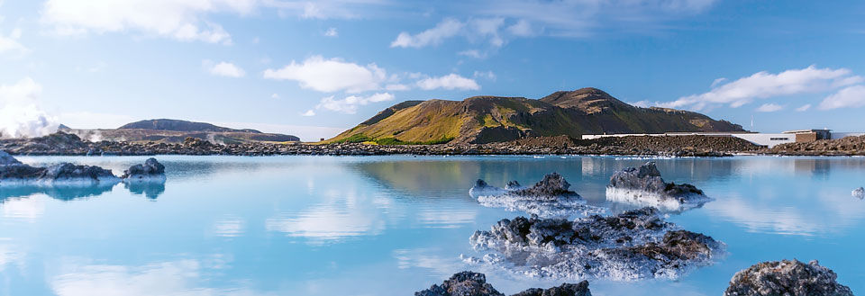 Ett storslaget landskap med en varm, turkosblå geotermisk vattenpool omgiven av vulkaniska klippor och gröna kullar.