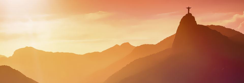 Den stora Kristusstatyn i solnedgången med vackra färger och silhuetter av bergskedjor.