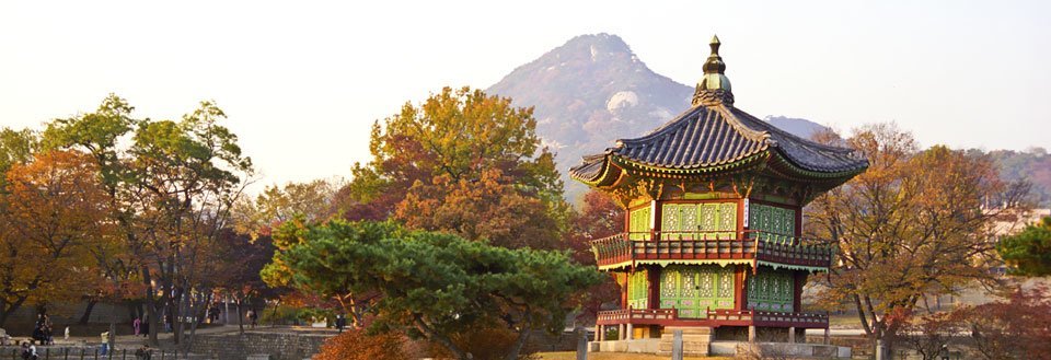 Ett traditionellt asiatiskt palats i Seoul omgivet av gyllene höstträd med berg i bakgrunden.