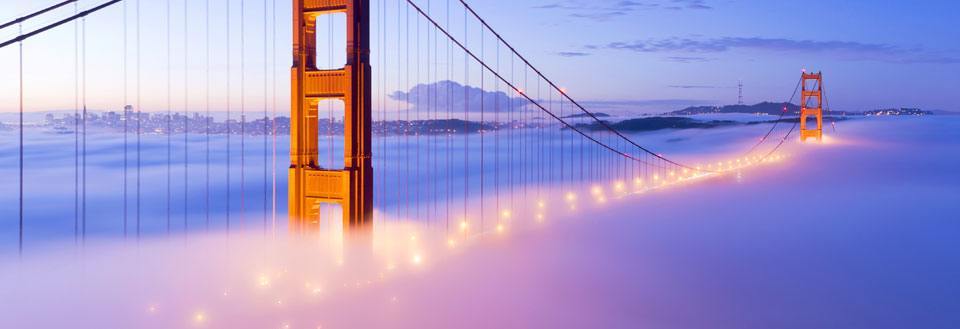 Golden Gate-bron i skymningen, upplyst och svävande över en tät dimma.