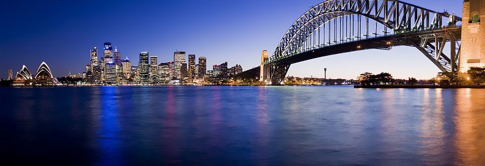 Sydneys silhuett med en berömd bågbro och speglingar i vattnet.