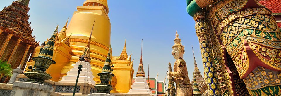 Grand Palace i Bangkok med gyllene stupor, färggranna mosaiker och traditionella statyer under en klarblå himmel.