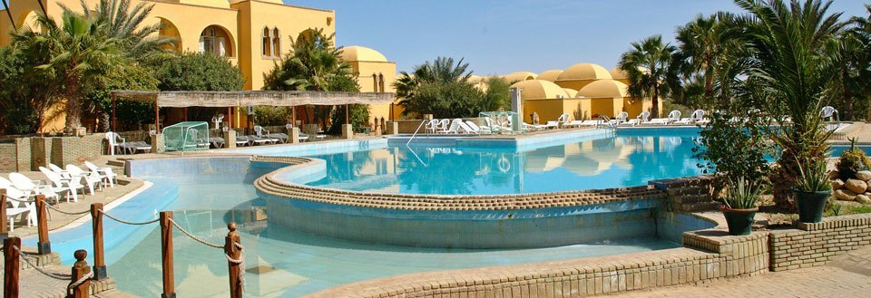 Lyxigt semesterställe med en stor pool, palmer och solstolar i solskenet.