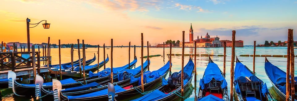 Solnedgång i Venedig med gondoler förtöjda vid träpålar, och San Giorgio Maggiore kyrkan i bakgrunden.