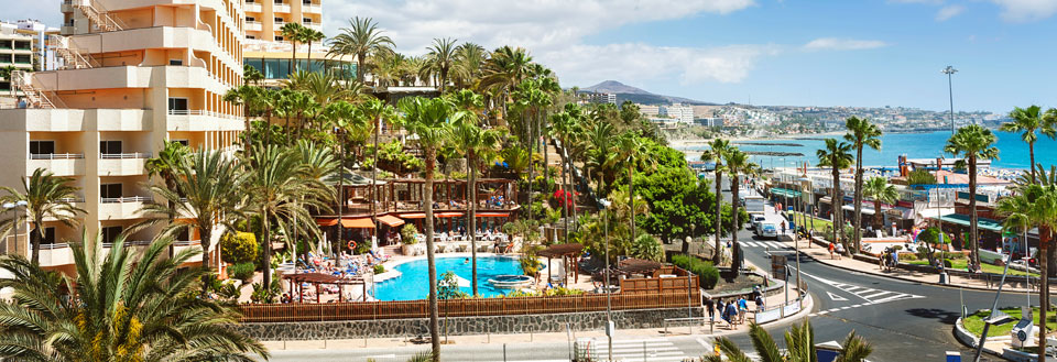 Livligt semesterresort med simbassäng, omgiven av palmer, och en klarblå himmel.