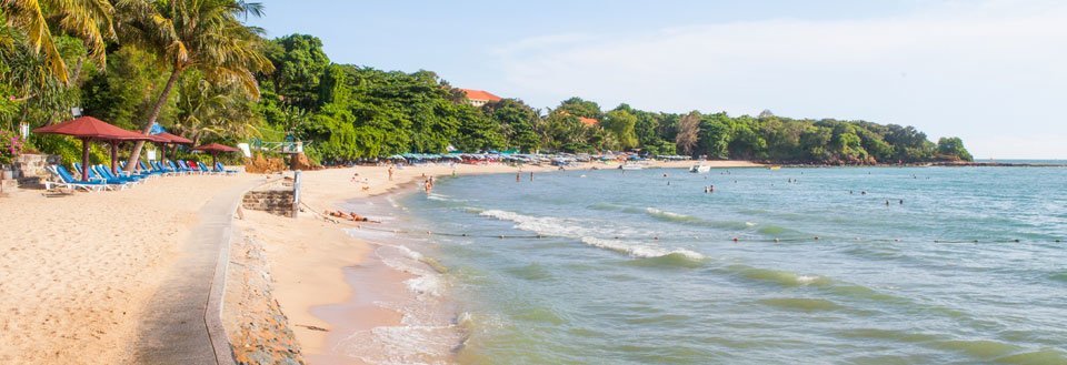 Strandvyen skildrar en solig dag med människor som avnjuter havet, sanden och solparasoller under tropiska träd.