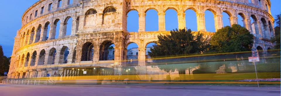 Colosseum i Pula, tagen i skymningen med lång exponering som visar ljusspår från en buss.