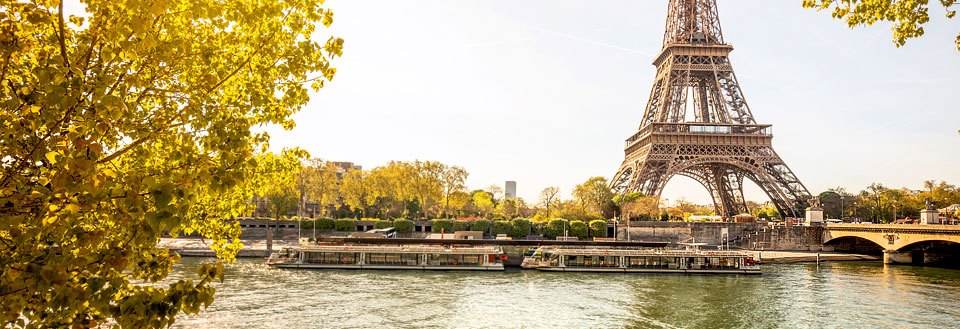 Eiffeltornet dominerar Paris silhuett vid Seine med en flodbåt, som glider förbi under klar himmel.