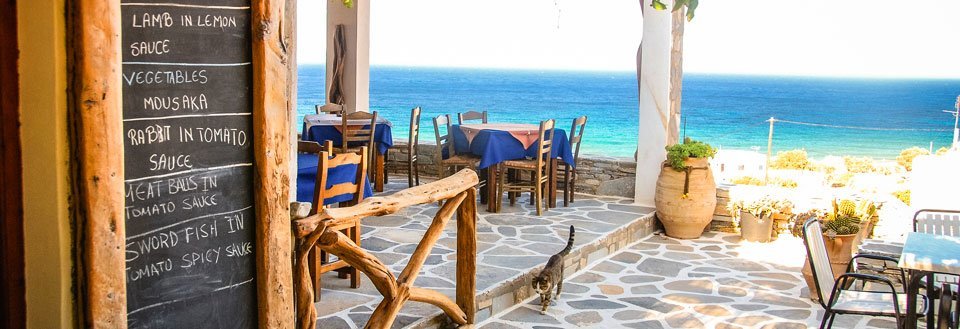 Mysig terrass vid havet med en meny på en tavla och stolar och bord.