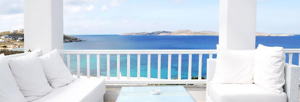 En vit balkong med bekväma soffor och en magnifik utsikt över det azurblå havet och en kustlinje.