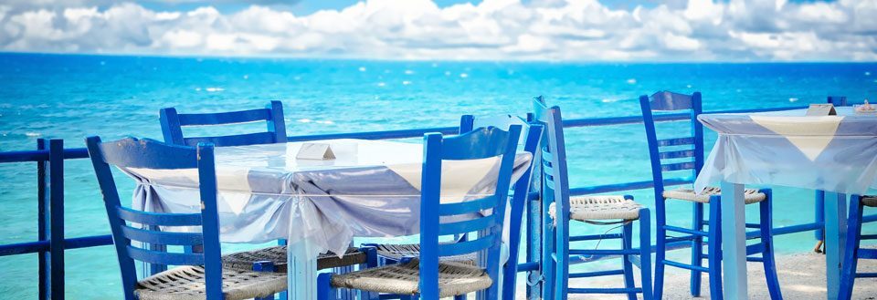 Ett trevligt utomhus serveringsområde med blå stolar framför en vacker havsutsikt.