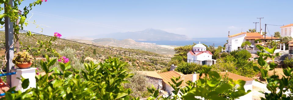 En idyllisk by med vita hus på Samos, grönområden och en kyrka, med berg i bakgrunden.