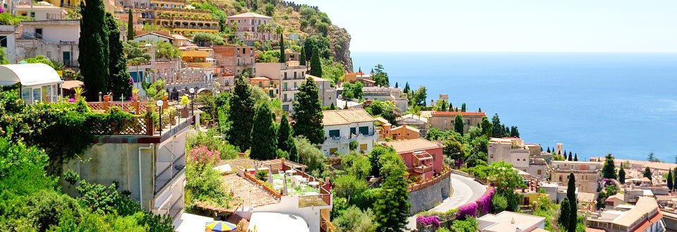 En pittoresk kuststad med tät bebyggelse, gröna terrasser och ett azurblått hav.