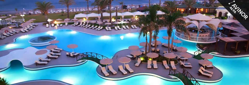 En lyxig semesteranläggning med en stor pool omgiven av solstolar och parasoller i skymningen.