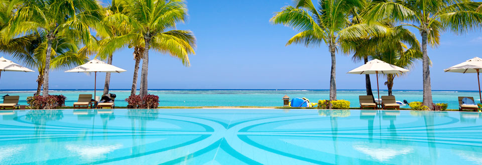 Lyxigt semesterort med pool framför en tropisk strand med palmer och parasoll.