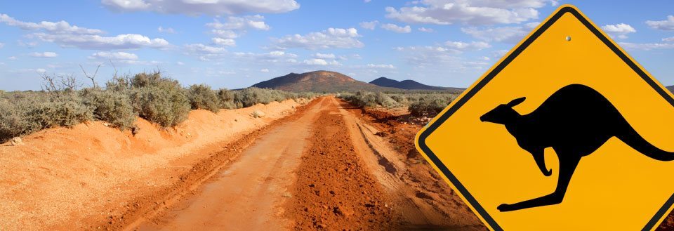 Röd jordväg som sträcker sig mot ett berg under en blå himmel, med varningsskylt för känguru.