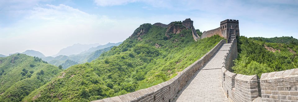 Panoramavy av Kinesiska muren som ringlar sig genom ett grönskande landskap.