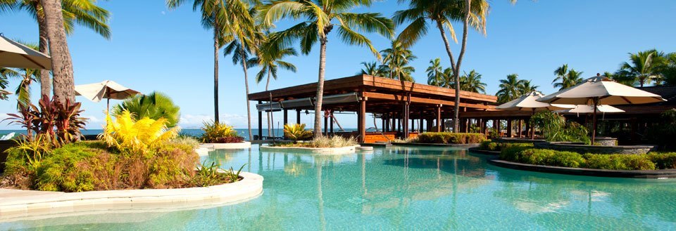 Lyxigt semesterort med simbassäng omgiven av palmträd och solstolar under parasoller.