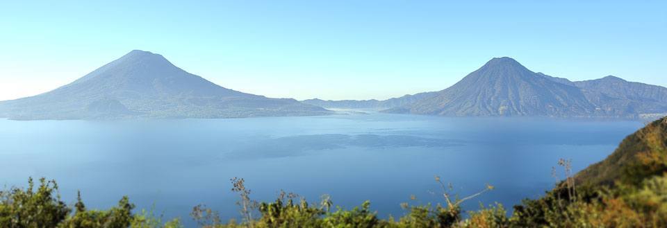 Panoramavy över en lugn sjö med kringliggande berg och en klarblå himmel.