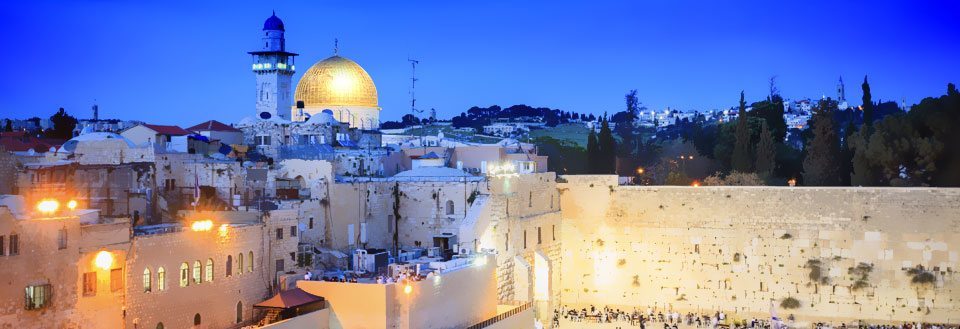 Kvällsbild av Västra muren och Klippdomen i Jerusalem, upplysta byggnader och människor vid muren.