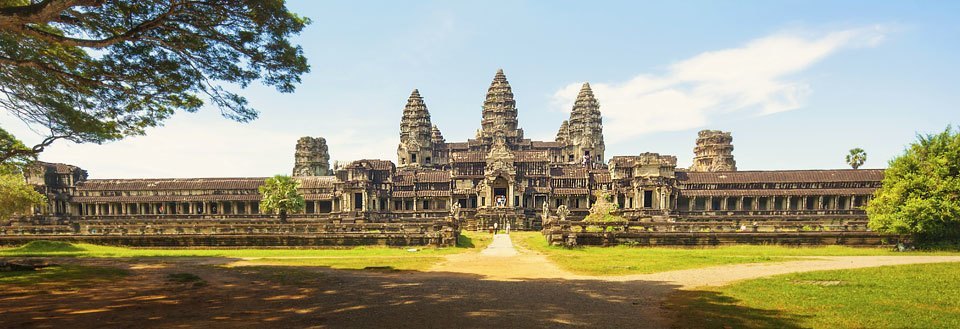 De majestätiska ruinerna av Angkor Wat i Kambodja, omgiven av gröna träd under en klar himmel.